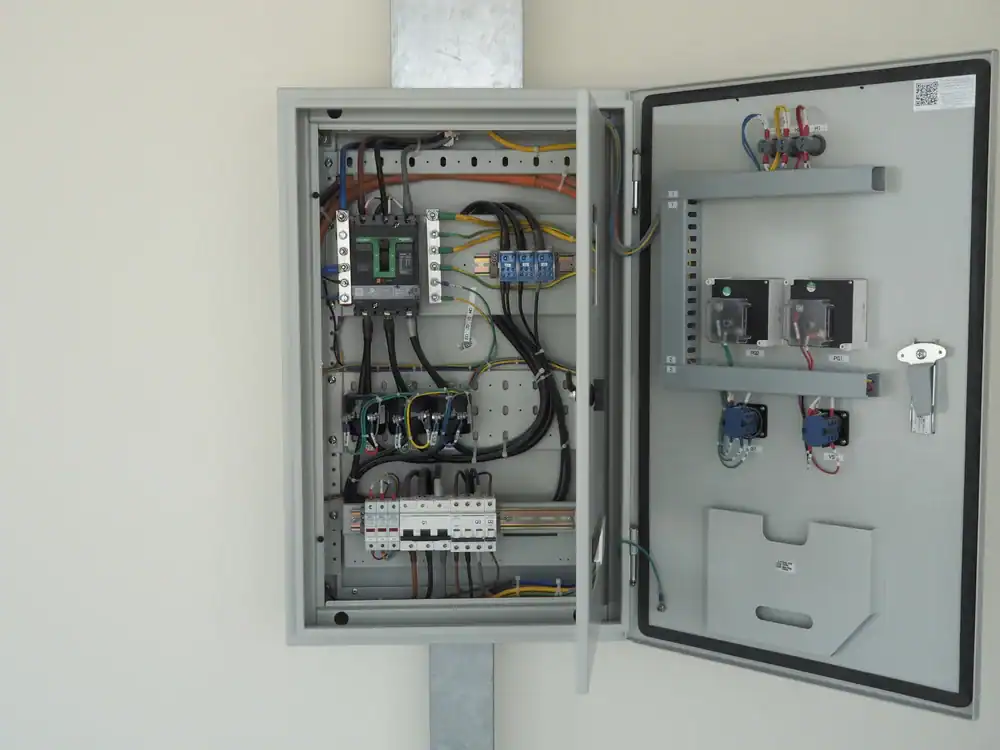 An open electrical control panel mounted on a wall in TX, showing various wires, switches, relays, circuit breakers, and electronic components neatly arranged inside the gray metal enclosure—ideal for any electrician Dallas and Fort Worth trusts.