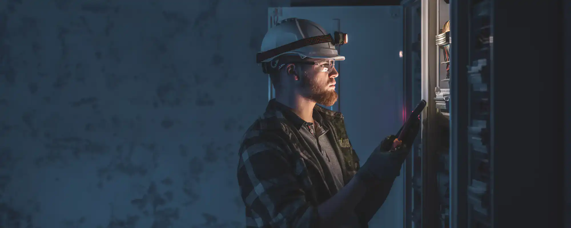 Emergency electrician repairing electrical panel at night, wearing safety gear with tools, Dallas County, Texas.